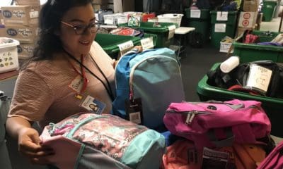 In a warehouse, a woman examines containers full of school backpacks