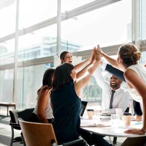 Shot of a group of businesspeople high fiving while sitting in a meeting.