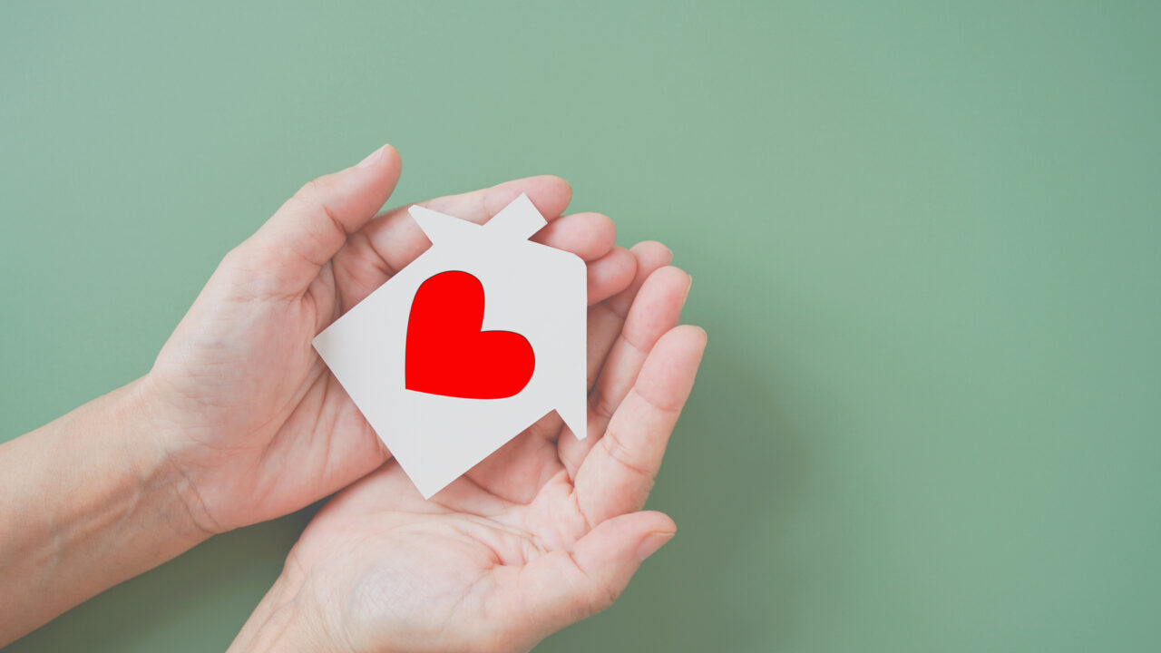 white house paper cut with red heart shape in hands on green background, homeless housing shelter and real estate , family house insurance, social distancing, home isolation concept